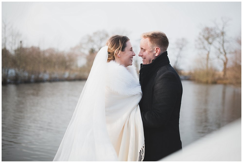  Bride and groom down by the lake at Styal Lodge on their snowy winter wedding day. 