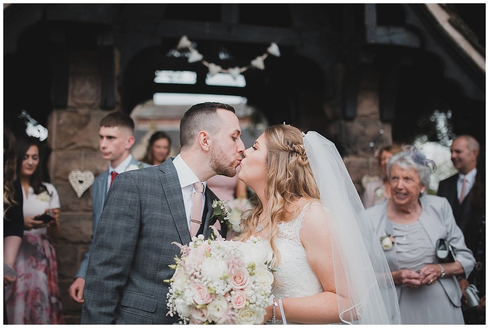  Pastel coloured wedding at Endon Church, Stoke-on-Trent. Bride and groom kiss at the Lych Gate outside this beautiful village church. 